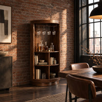 Tall cylinder bar cabinet with a glass rail on top and open cubbies below in an industrial loft dining room with exposed brick