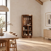 Tall cylinder bar cabinet with a glass rail on top and open cubbies below in a bright open plan dining room