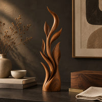 Corner detail of tall flame sculpture of layered leaf blades rising from a smooth base beside wood, brass and linen samples