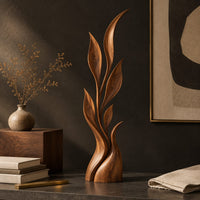 Corner detail of wood sculpture of a slim leafy stem with pointed leaves and a sculpted base beside wood, brass and linen samples