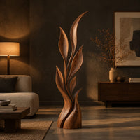 Wood sculpture of a slim leafy stem with pointed leaves and a sculpted base in a dark living room at golden hour