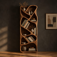 Tall narrow wooden bookshelf with slanted dividers and flowing open cubbies in a dark studio against a charcoal plaster wall