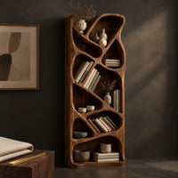 Corner detail of tall narrow wooden bookshelf with slanted dividers and flowing open cubbies beside wood, brass and linen samples