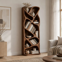 Tall narrow wooden bookshelf with slanted dividers and flowing open cubbies in a Scandinavian living room with white walls