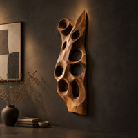 Tall carved wood wall art with oval hollows and a pointed top on a dark charcoal plaster wall