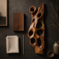 Detail of tall carved wood wall art with oval hollows and a pointed top beside wood, brass and linen samples