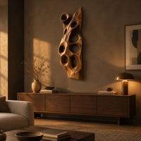 Tall carved wood wall art with oval hollows and a pointed top above a low console in an evening living room