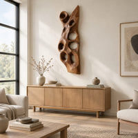 Tall carved wood wall art with oval hollows and a pointed top above a light oak sideboard in daylight