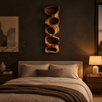 Tall wooden wall sculpture with five stacked organic openings above a bed in a dusk lit bedroom