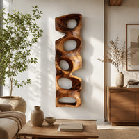 Tall wooden wall sculpture with five stacked organic openings in a bright sunroom with green plants