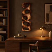 Tall wooden wall sculpture with five stacked organic openings above a desk in a dark study corner