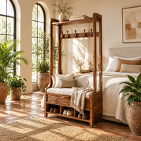 Tall wood storage bench with coat hooks and three open cubbies in a bright bedroom with arched windows and plants