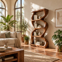 Tall bookshelf with wavy sides, four open shelves and a thick organic frame in a bright living room with arched windows and plants