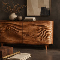 Corner detail of sideboard with four wave carved doors and tapered legs beside wood, brass and linen samples