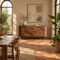 Sideboard with four wave carved doors and tapered legs in a bright dining room with arched windows and plants