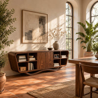 Tapered sideboard with open cubbies on both sides and a wavy base in a bright dining room with arched windows and plants