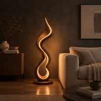 Floor lamp made of one flowing ribbon that ends in a teardrop loop in a dark living room at golden hour