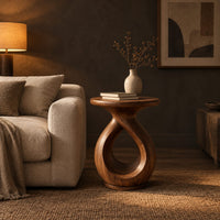 Round side table on a looped teardrop pedestal with a flat disc base in a dark living room at golden hour