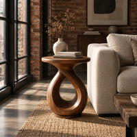 Round side table on a looped teardrop pedestal with a flat disc base in an industrial loft living room with exposed brick