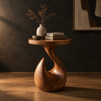 Circular side table on a teardrop pedestal with a swirling neck in a dark studio against a charcoal plaster wall