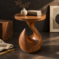 Corner detail of circular side table on a teardrop pedestal with a swirling neck beside wood, brass and linen samples