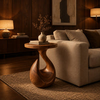 Circular side table on a teardrop pedestal with a swirling neck in an evening living room with walnut wall paneling