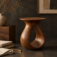 Corner detail of teardrop side table with a flared top and an open loop body beside wood, brass and linen samples