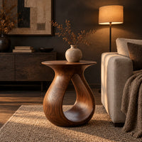 Teardrop side table with a flared top and an open loop body in a dark living room at golden hour
