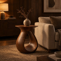 Teardrop side table with a flared top and an open loop body in an evening living room with walnut wall paneling