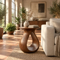 Teardrop side table with a flared top and an open loop body in a bright living room with arched windows and plants