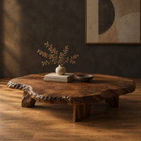 Low coffee table with a thick live edge slab top on short chunky legs in a dark studio against a charcoal plaster wall