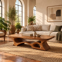 Thick slab coffee table with a carved cutout base in a bright living room with arched windows and plants