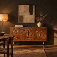 Three door sideboard with carved face reliefs and tapered angled legs in a dark dining room at golden hour