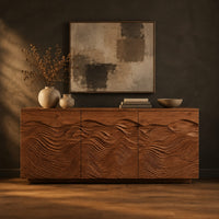 Low sideboard with three doors carved in flowing waves on a plinth base in a dark studio against a charcoal plaster wall