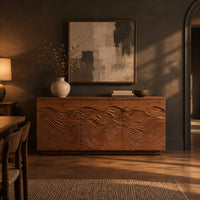 Low sideboard with three doors carved in flowing waves on a plinth base in a dark dining room at golden hour