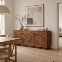 Low sideboard with three doors carved in flowing waves on a plinth base in a Scandinavian dining room with white walls