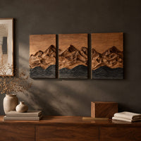 Detail of three panel wood wall art with a carved mountain range above dark waves beside wood, brass and linen samples