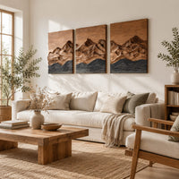 Three panel wood wall art with a carved mountain range above dark waves in a bright sunroom with green plants