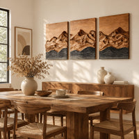 Three panel wood wall art with a carved mountain range above dark waves beside a dining table in natural light
