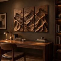 Three panel carved mountain relief wall art with a sun disc above a desk in a dark study corner
