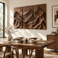 Three panel carved mountain relief wall art with a sun disc beside a dining table in natural light