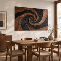 Three panel spiral wall art with a carved black swirl on warm wood beside a dining table in natural light