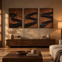Set of three framed wood panels carved with a dark winding river above a low console in an evening living room
