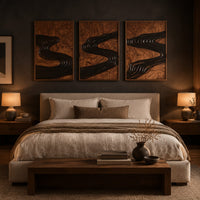 Set of three framed wood panels carved with a dark winding river above a bed in a dusk lit bedroom