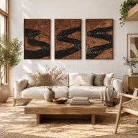 Set of three framed wood panels carved with a dark winding river in a bright sunroom with green plants