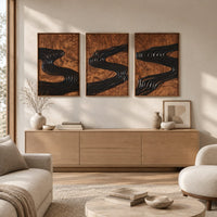 Set of three framed wood panels carved with a dark winding river above a light oak sideboard in daylight