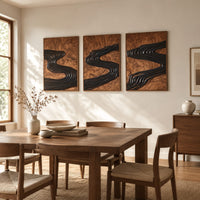 Set of three framed wood panels carved with a dark winding river beside a dining table in natural light