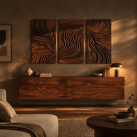 Three panel wall art with flowing carved grain pattern above a low console in an evening living room