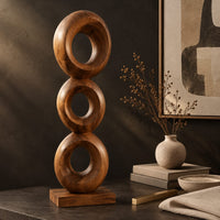 Corner detail of stacked three ring sculpture with open centers on a flat plinth beside wood, brass and linen samples