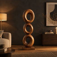 Stacked three ring sculpture with open centers on a flat plinth in a dark living room at golden hour